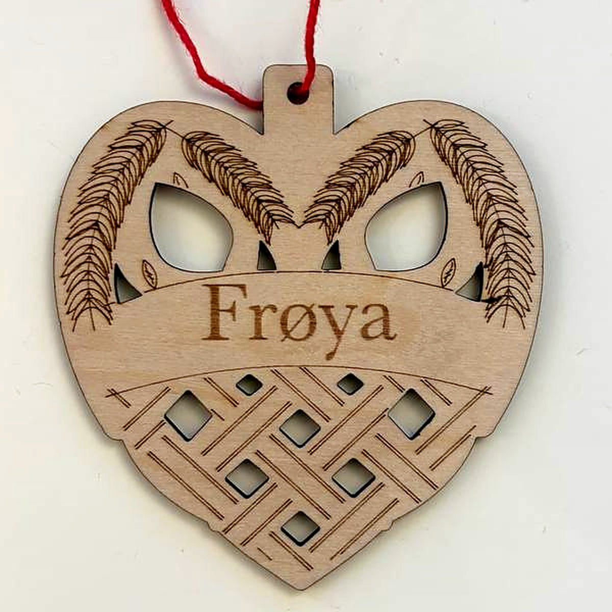 Close view of the woven heart ornament: the engraved name Frøya above a cut-out woven pattern, with engraved wheat sprigs